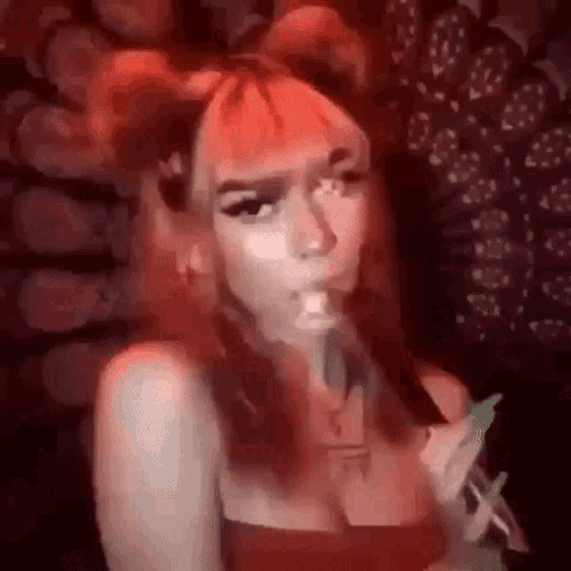 a woman with red hair is smoking a cigarette while wearing a red dress .