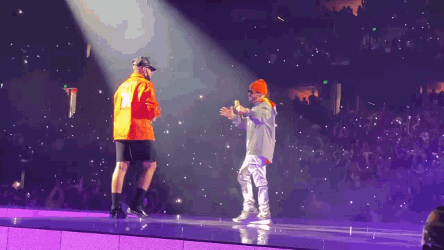 two men on a stage with one wearing an orange jacket with the number 12 on it
