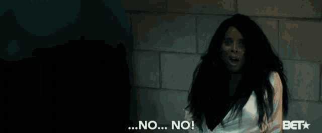 a woman in a white shirt says " no " in front of a brick wall
