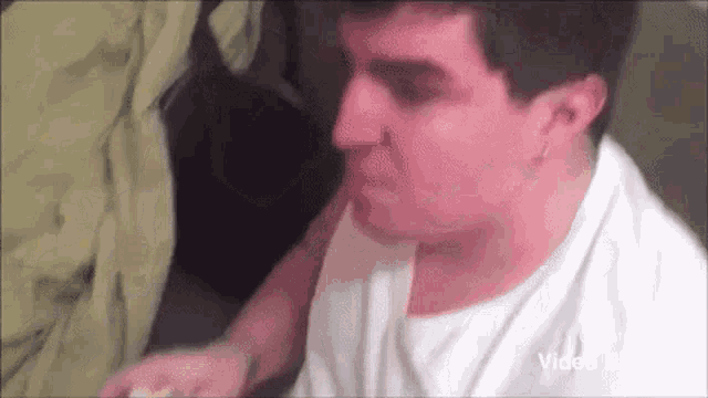 a man in a white shirt is sitting on a couch and eating a sandwich .