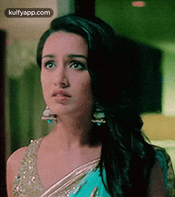 a close up of a woman wearing a saree and earrings making a funny face .