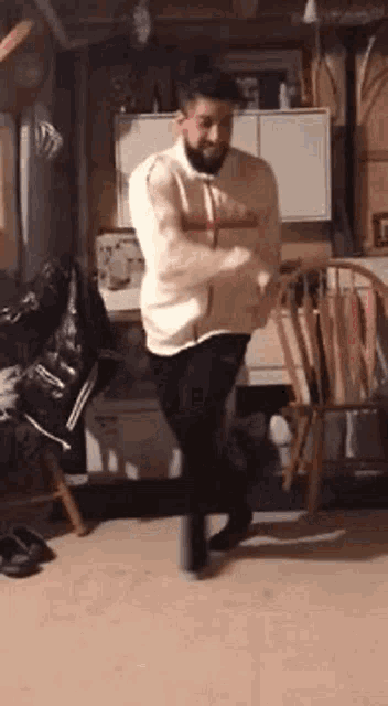 a man with a beard is dancing in a room with chairs .