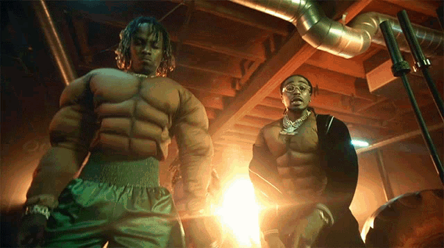 two men in muscle costumes are standing in a dark room