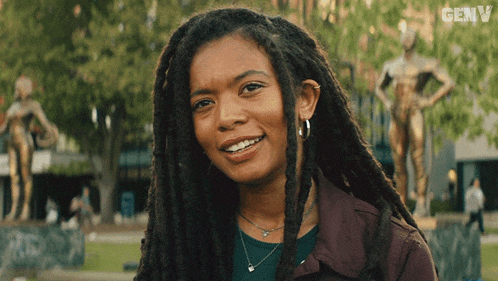 a woman with dreadlocks is smiling in front of a statue and the word genv is on the bottom right