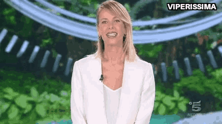 a woman in a white jacket is smiling in front of a green background with the words viperissima on the bottom right