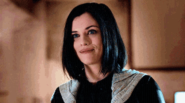 a woman with short black hair is smiling and wearing a black jacket .