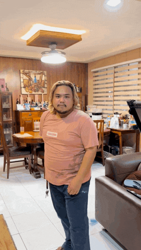 a man standing in a living room wearing a pink shirt that says supreme