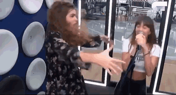 two women are singing into microphones in front of a mirror .