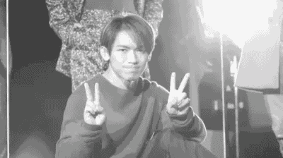 a young man is giving a peace sign with his hands in a black and white photo .