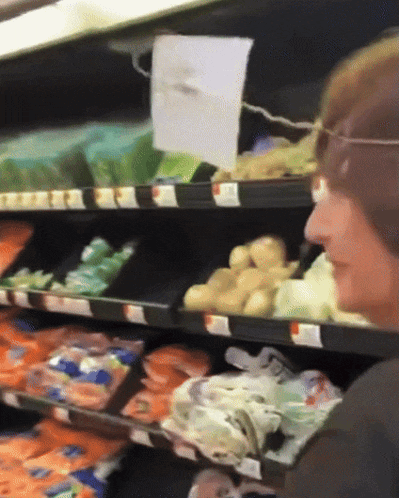 a woman in a grocery store looking at potatoes on a shelf