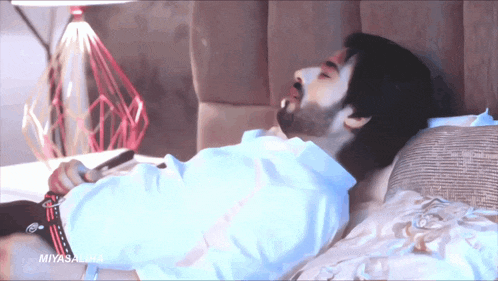 a man with a beard is laying on a bed holding a cell phone