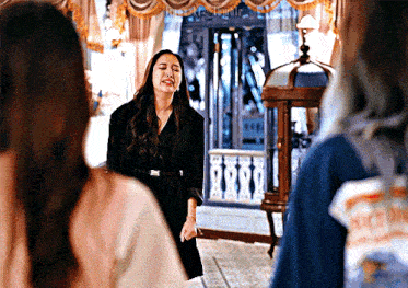 a woman in a black dress is standing in a room with other people .