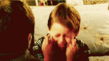 a little boy is sitting on a couch with his hands on his face .