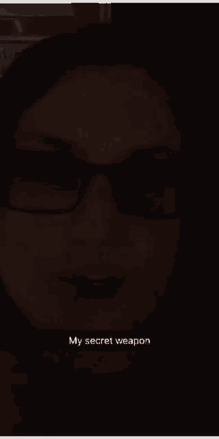 a woman wearing glasses says " my secret weapon " in the dark