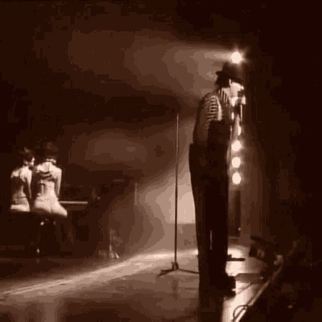 a man is singing into a microphone on a stage while a woman sits at a piano .