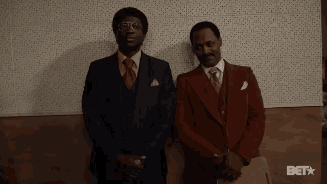 two men in suits are standing next to each other in front of a wall that says bet on it