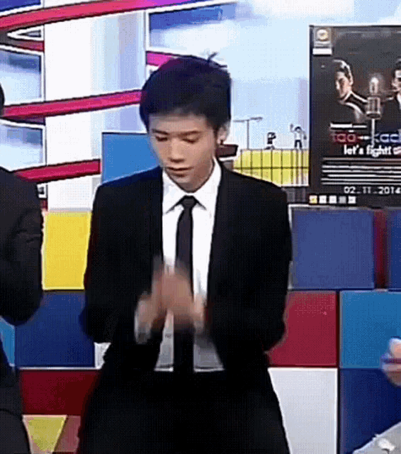 a man in a suit and tie is clapping his hands in front of a sign that says " let 's fight "