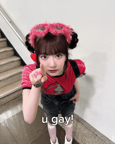 a girl wearing a pink headband and a red shirt is pointing at the camera with the caption u gay