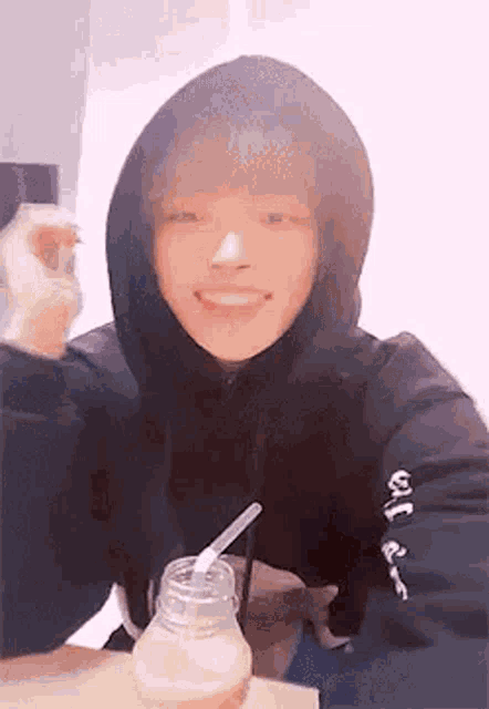 a young man in a hoodie is sitting at a table drinking from a bottle .