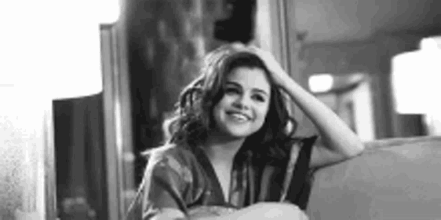 a black and white photo of a woman sitting on a couch and smiling .