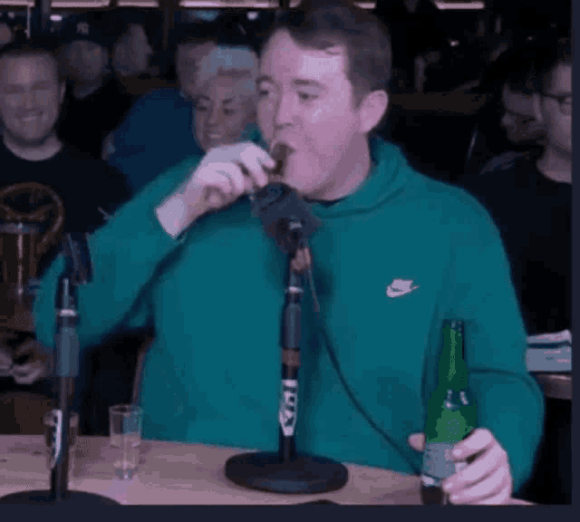 a man in a green nike sweatshirt is drinking a beer