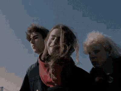 a group of people standing next to each other with their hair blowing in the wind