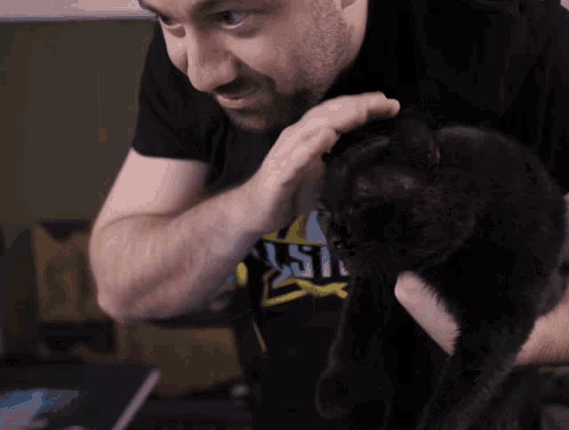 a man petting a black cat while wearing a shirt that says ' waste ' on it