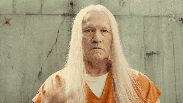 a man with long white hair has his fist up in front of a wall with an x on it
