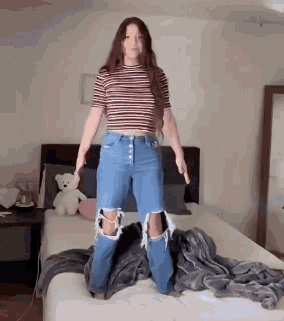a woman in ripped jeans is standing on a bed