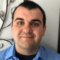a man in a blue shirt is smiling for the camera in front of a wall .