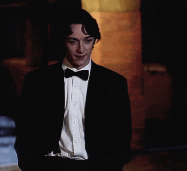 a man in a tuxedo with a bow tie is standing in front of a brick wall