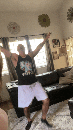 a man dancing in a living room with a stitch shirt on