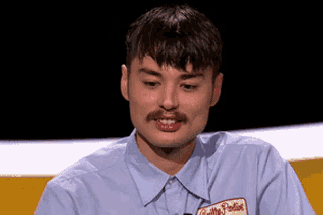 a man with a mustache is wearing a blue shirt with a name tag that says gillette