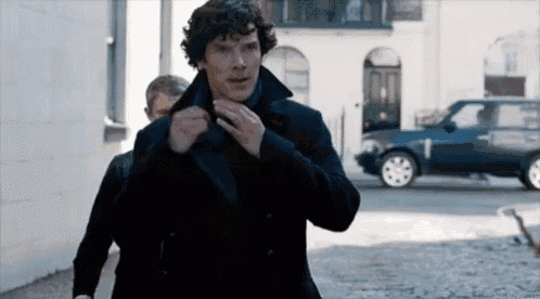 a man in a black coat is adjusting his tie while walking down the street .