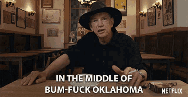 a man sitting at a table with a cigarette in his hand says in the middle of bum-fuck oklahoma netflix