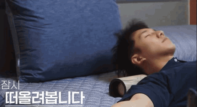 a man is laying on a bed with his eyes closed and a blue pillow behind him with korean writing on it