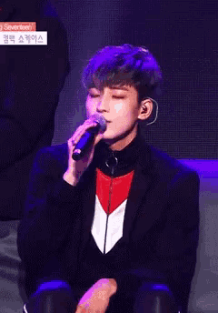 a man in a suit is singing into a microphone with purple lights behind him