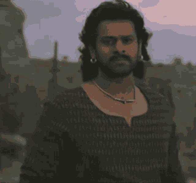 a man with a beard and earrings is wearing a necklace and a sweater .