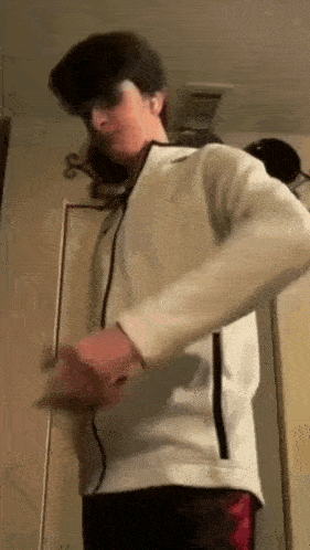 a young man is standing in front of a door wearing a white jacket .