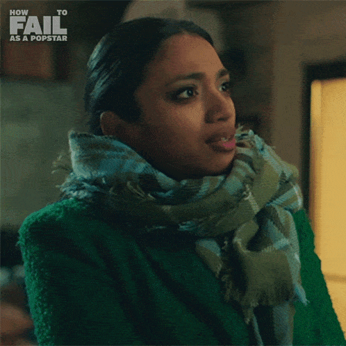 a woman wearing a green coat and scarf is smiling and says what