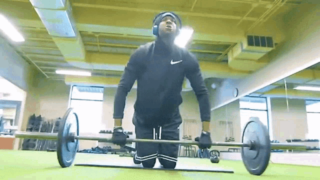 a man wearing headphones and a nike shirt is lifting a barbell in a gym