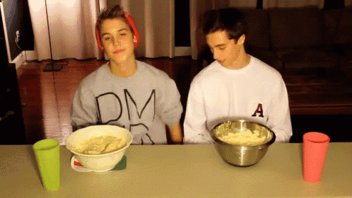 a man wearing a dm sweatshirt sits at a table with a bowl of food in front of him