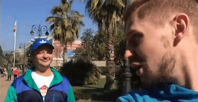two men are standing next to each other in a park and talking to each other .