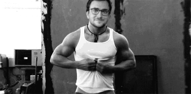 a man wearing glasses and a white tank top is standing in front of a wall .