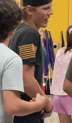 a man in a black shirt with a gold stripe on the sleeve is standing in a crowd of people .