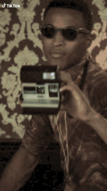 a man wearing sunglasses holds a polaroid camera