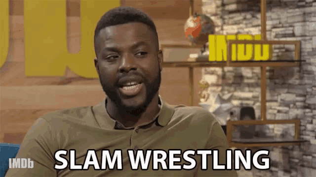 a man with a beard says slam wrestling in front of a brick wall