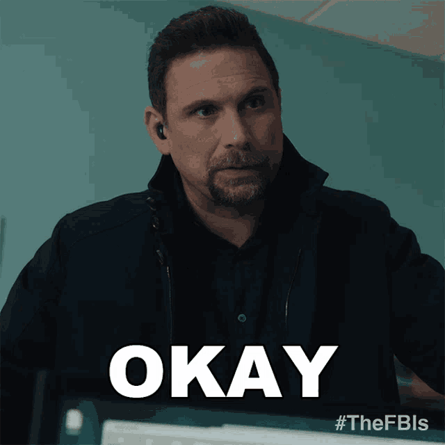a man wearing ear buds says okay in front of a blue wall