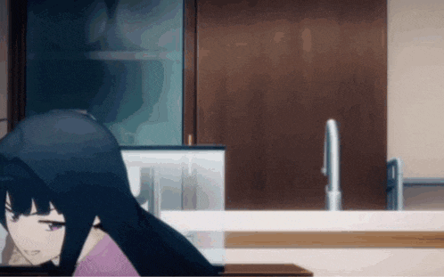 a girl with long black hair is sitting in a kitchen looking at a laptop .
