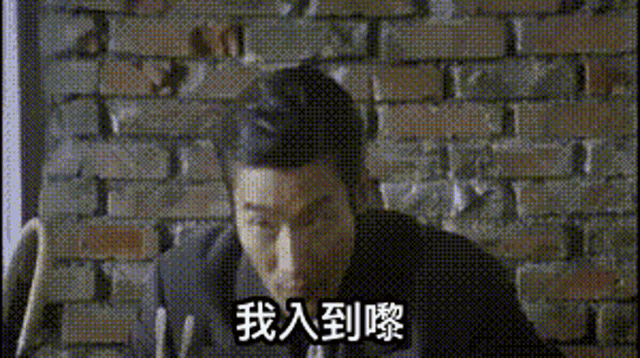 a man in a suit is sitting in front of a brick wall with chinese writing on it .